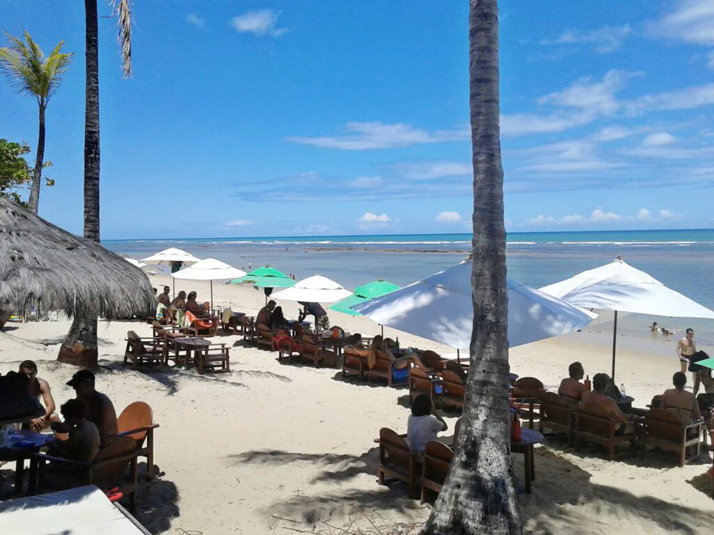 Pessoas sentadas embaixo do guarda-sol em frente ao mar de Praia do Mucugê em Arraial d’Ajuda na Bahia